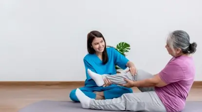 Caregiver helping a senior woman with gentle leg exercises at home